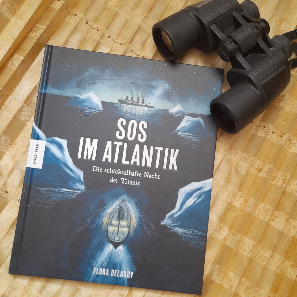 Bilderbuch "SOS im Atlantik: die schicksalhafte Nacht der Titanic" von Flora Delargy. Das gemalte Titelbild zeigt ein kleines Schiff, das bei Nacht ins Eismeer fährt, am Horizont die Silhouette der Titanic. Das Buch liegt auf einem gelben Stoff, ein Fernglas liegt als Requisit daneben.