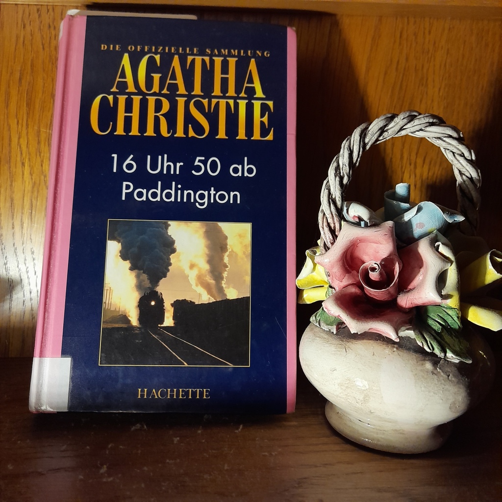 Neben einer kleinen Keramik-Vase mit einem Blumenstrauß ebenfalls aus Keramik steht das Buch "16 Uhr 50 ab Paddington" von Agatha Christie