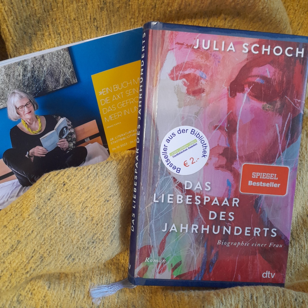 Auf einer gelben Decke liegen das Buch "Das Liebespaar des Jahrhunderts: Biographie einer Frau" von Julia Schoch und das Programmheft der Literaturtage 2023