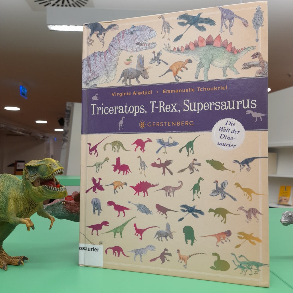 Kinderbilderbuch "Triceratops, T-Rex, Supersaurus". Neben dem Buch die Spielzeugfigur eines Tyrannosaurus Rex