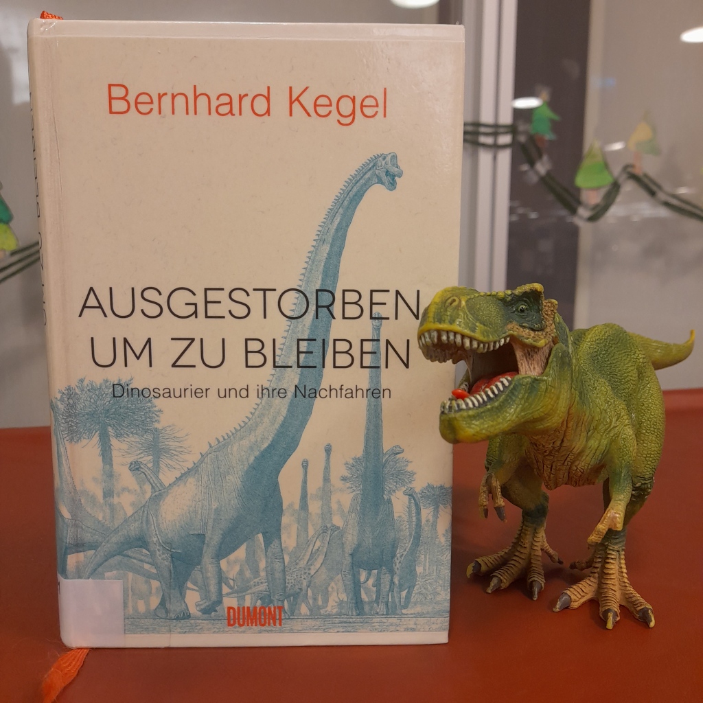 Sachbuch "Ausgestorben, um zu bleiben" von Bernhard Kegel. Neben dem Buch steht ein Tyrannosaurus mit aufgerissenem Maul (als Plastik-Spielfigur)